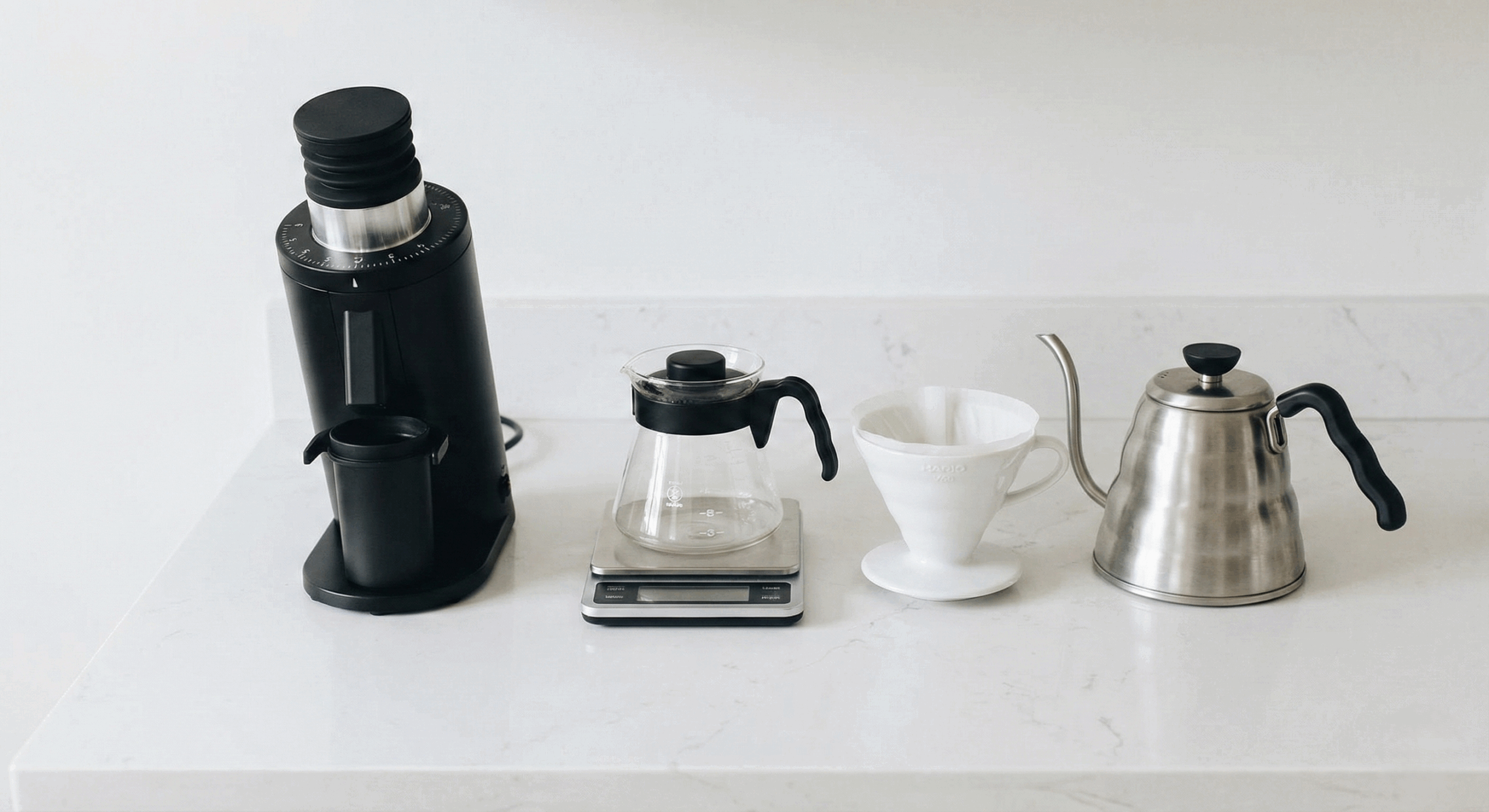 Essential home coffee brewing setup featuring a manual burr grinder, digital scale, dripper, and gooseneck kettle on a minimalist counter.