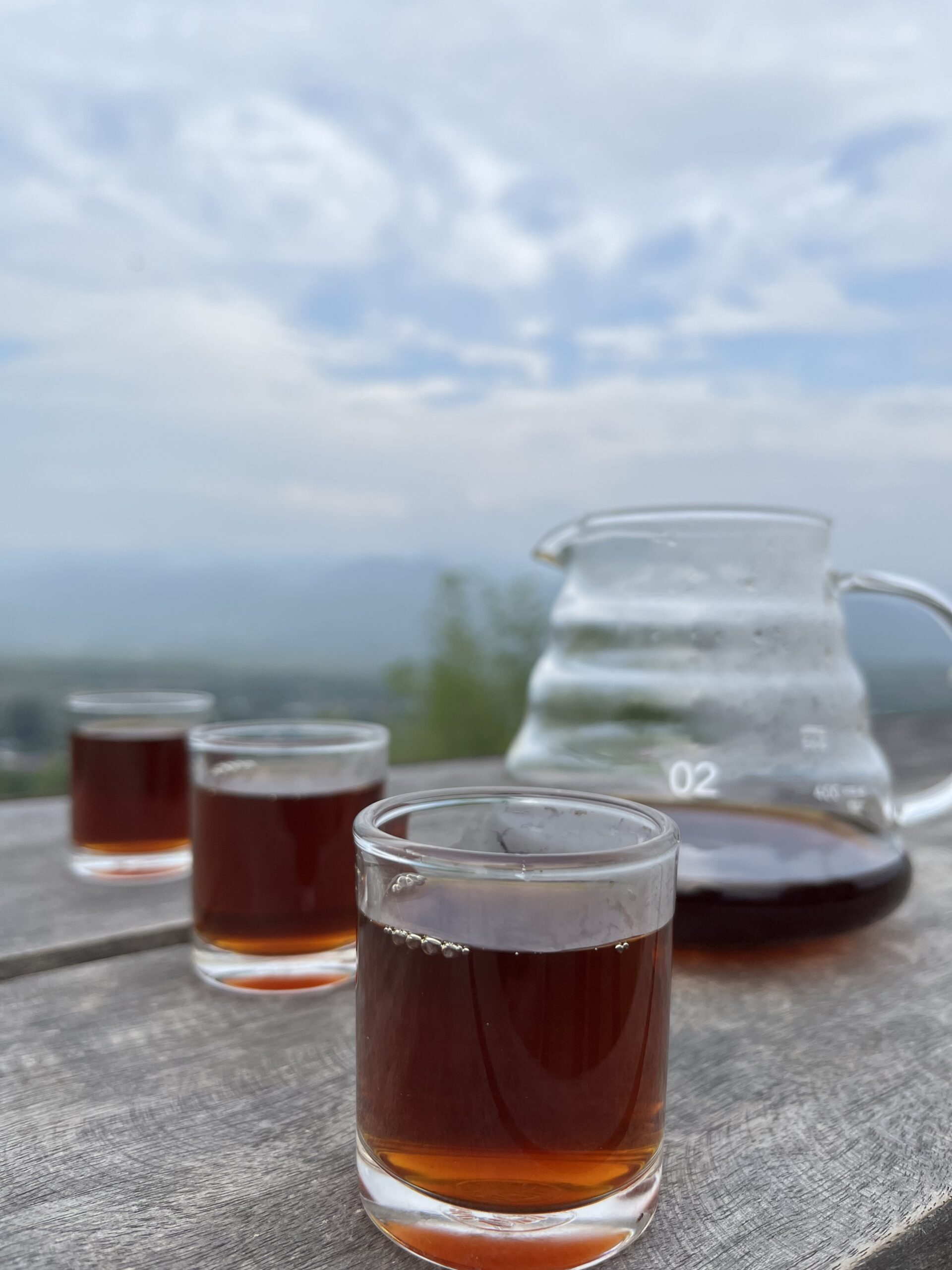 A glass of brewed specialty coffee overlooking the layered, mist-covered mountains of Mae Hong Son, Thailand, featuring the origin of Rodlamoon coffee beans.
