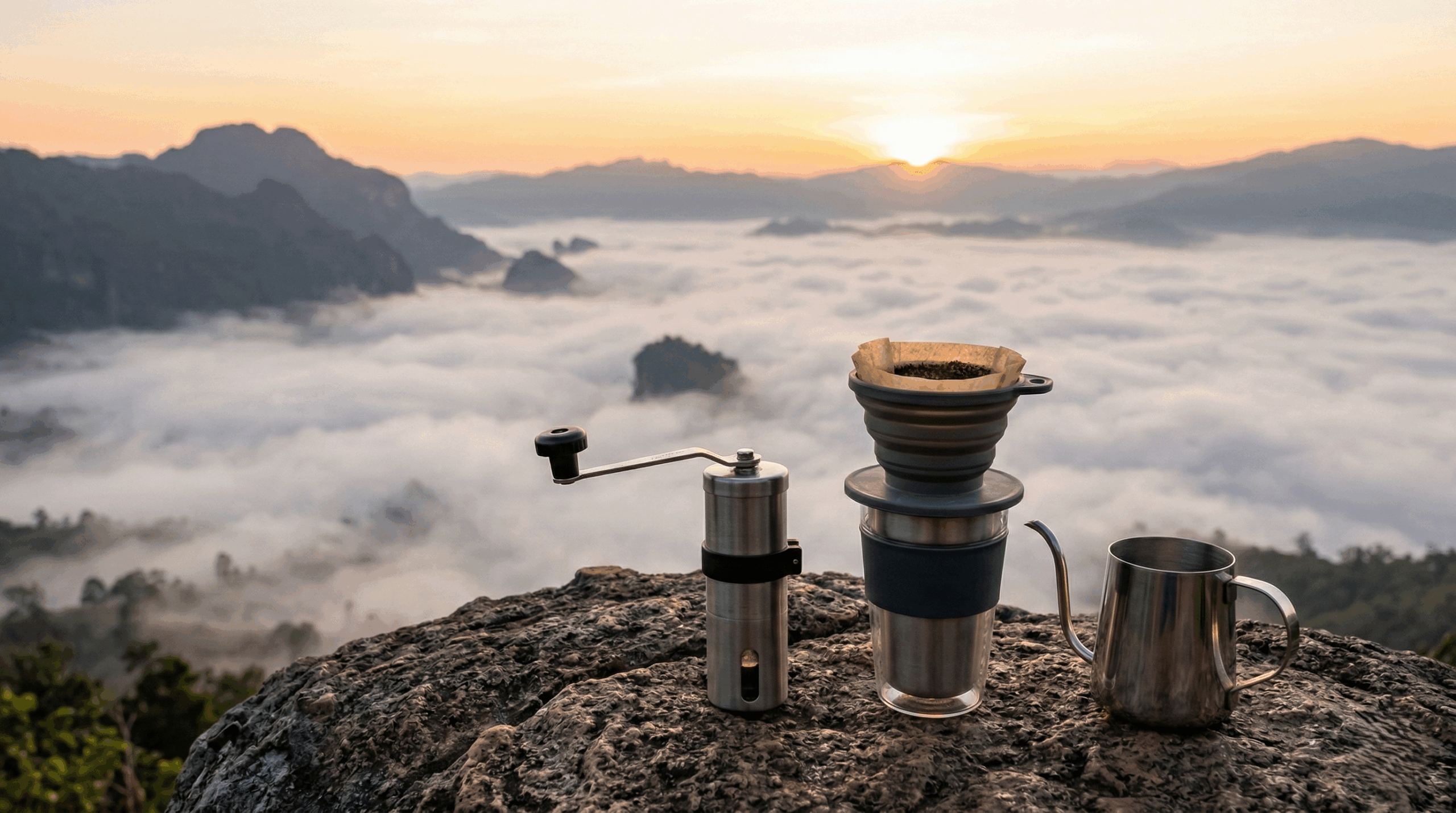 A compact manual coffee grinder and a travel dripper set on a rock overlooking a misty valley in Mae Hong Son.